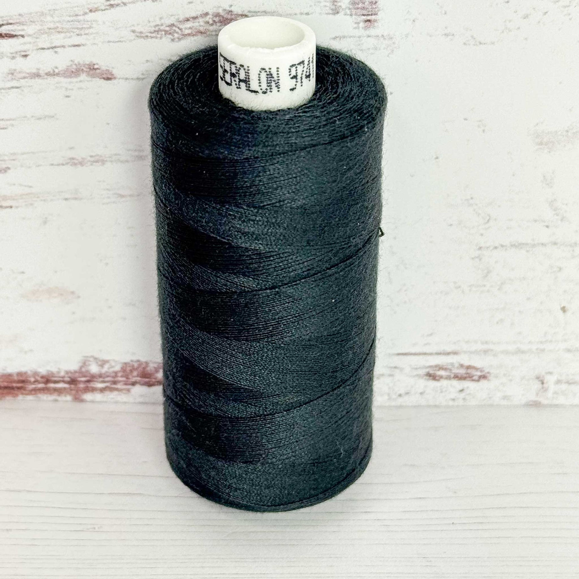Spool of dark thread with a visible brand label on a light wooden background