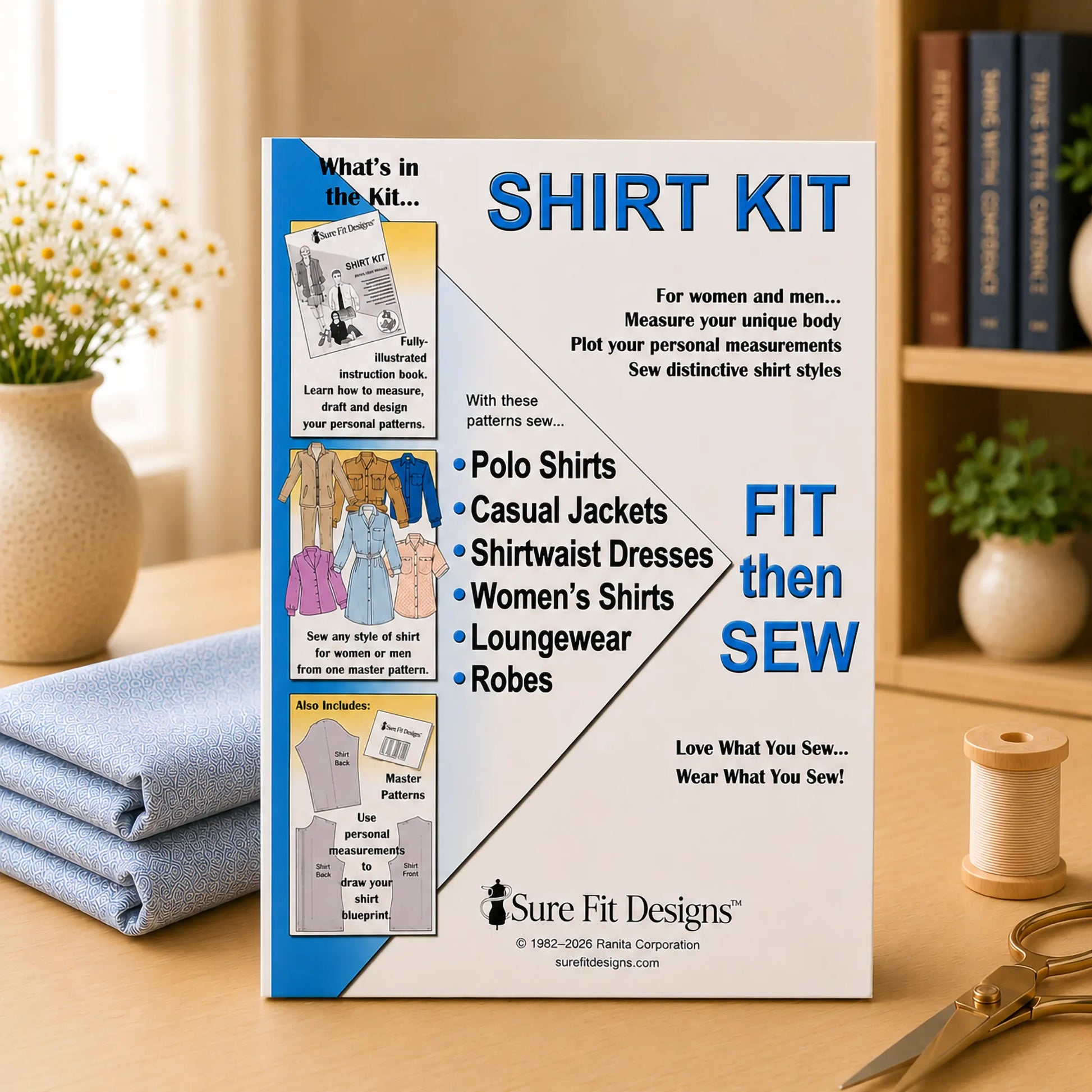 A 'Shirt Kit' sewing pattern box by Sure Fit Designs stands on a wooden table, surrounded by a folded blue shirt, a spool of thread, scissors, and books in the background.