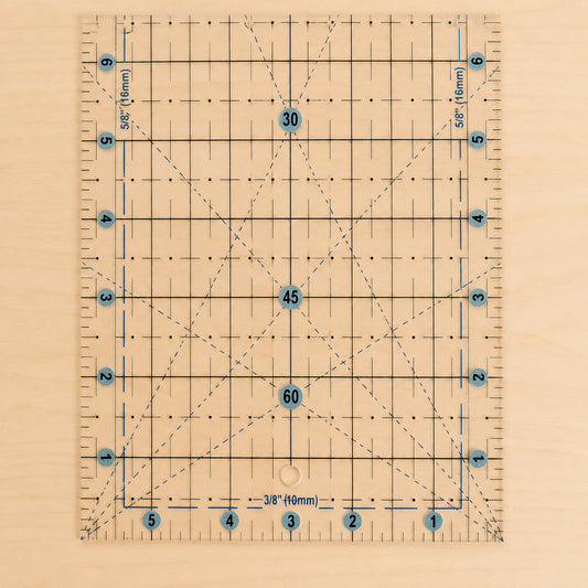 A clear acrylic quilting ruler with a light wood backing, featuring a grid system, diagonal guide lines, and blue circular markings with numbers.
