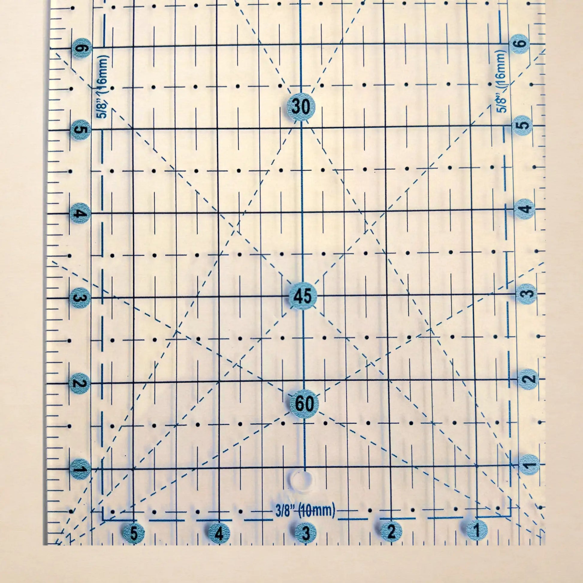 A clear square quilting ruler with blue grid lines, measurement markings, and numbered intersection points from 1 to 6, shown on a light beige background.