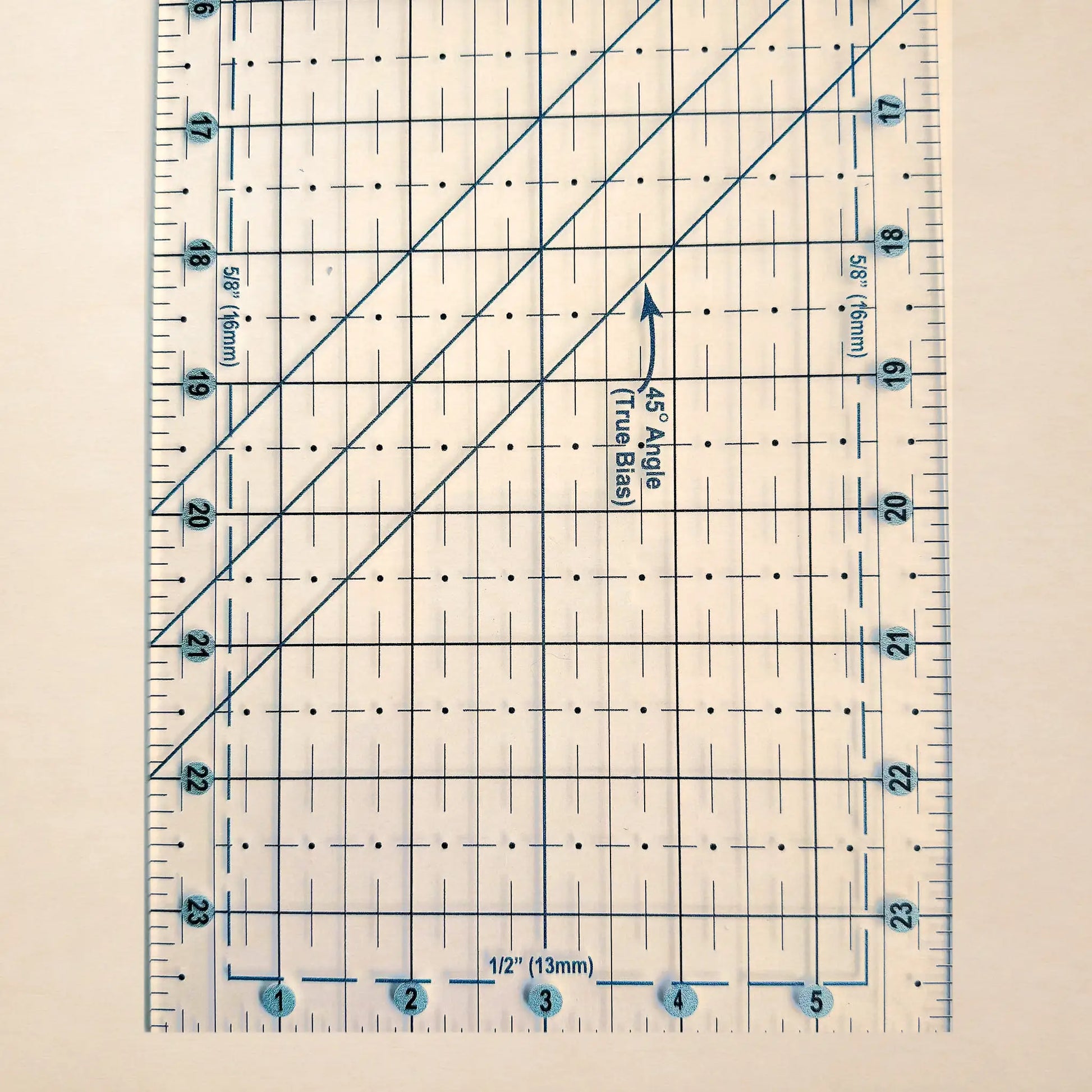 A clear quilting ruler with blue printed grid lines, measurement markings, and diagonal guide lines, shown on a light beige background.