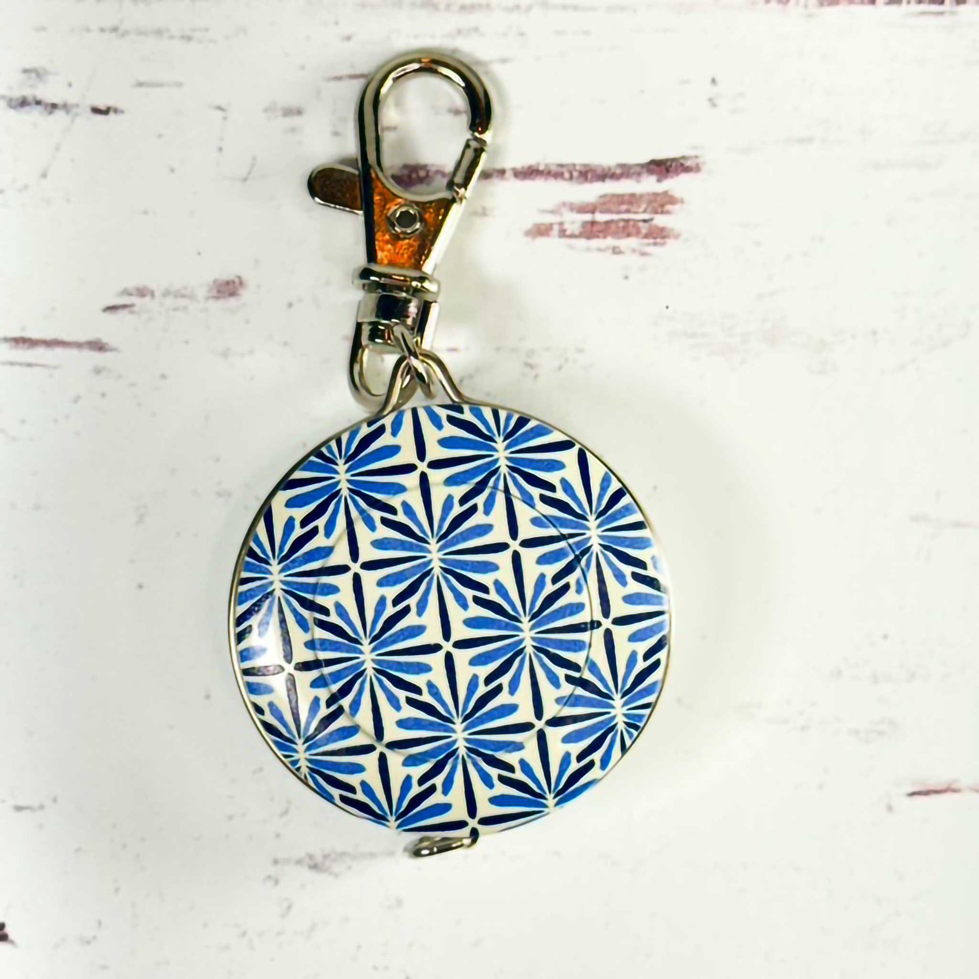 blue and white circular tape measure/keychain with a metal clasp on a textured white background