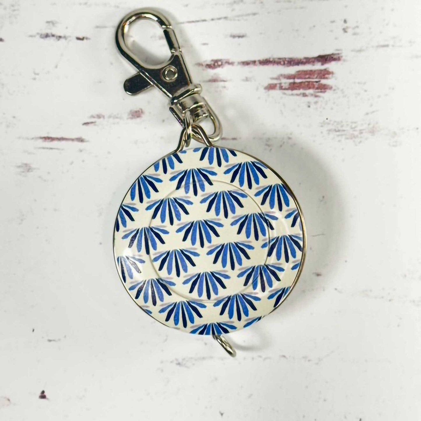 blue and white circular tape measure/keychain with a metal clasp on a textured white background
