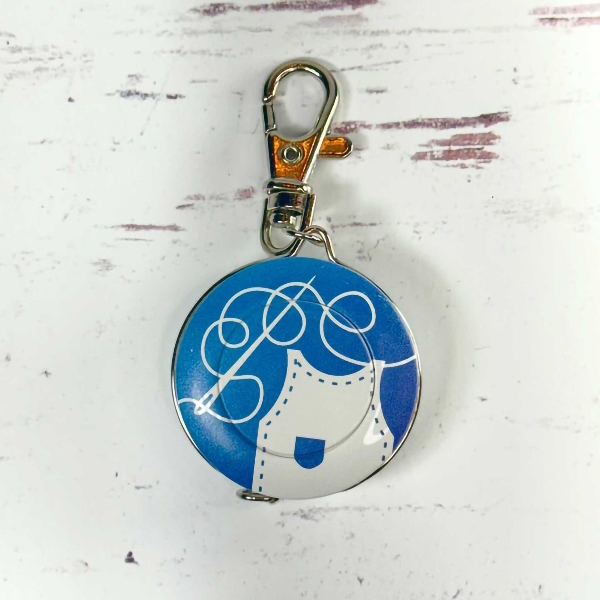 Round blue and white tape measure keychain with a design on a light gray background