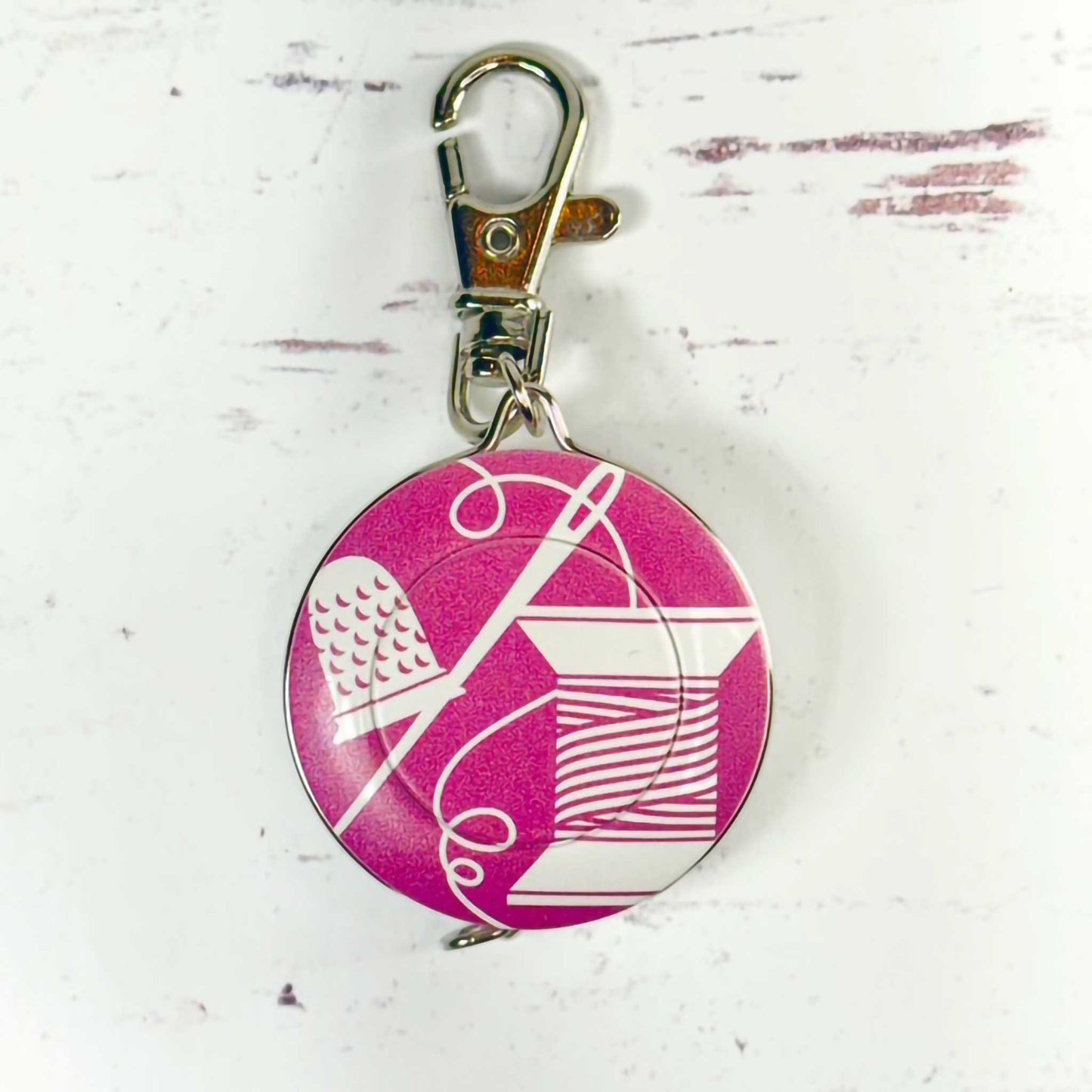 Pink tape measure/keychain with sewing symbols on a white background