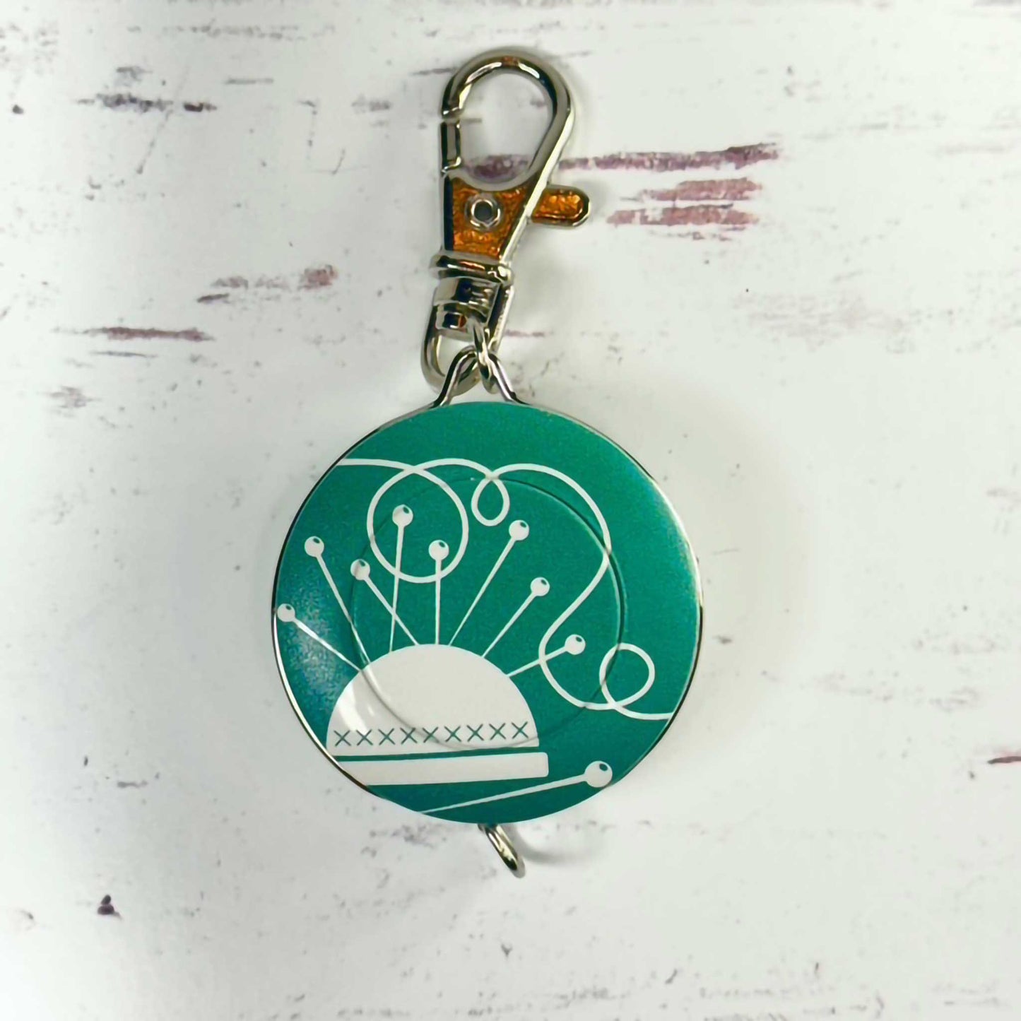 Teal retractable tape measure/keychain with white design on a white background