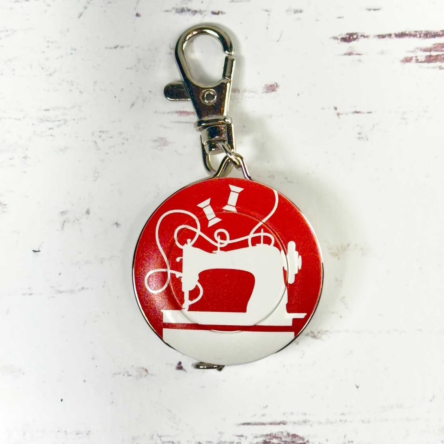 round tape measure/keychain with sewing machine design on a red background