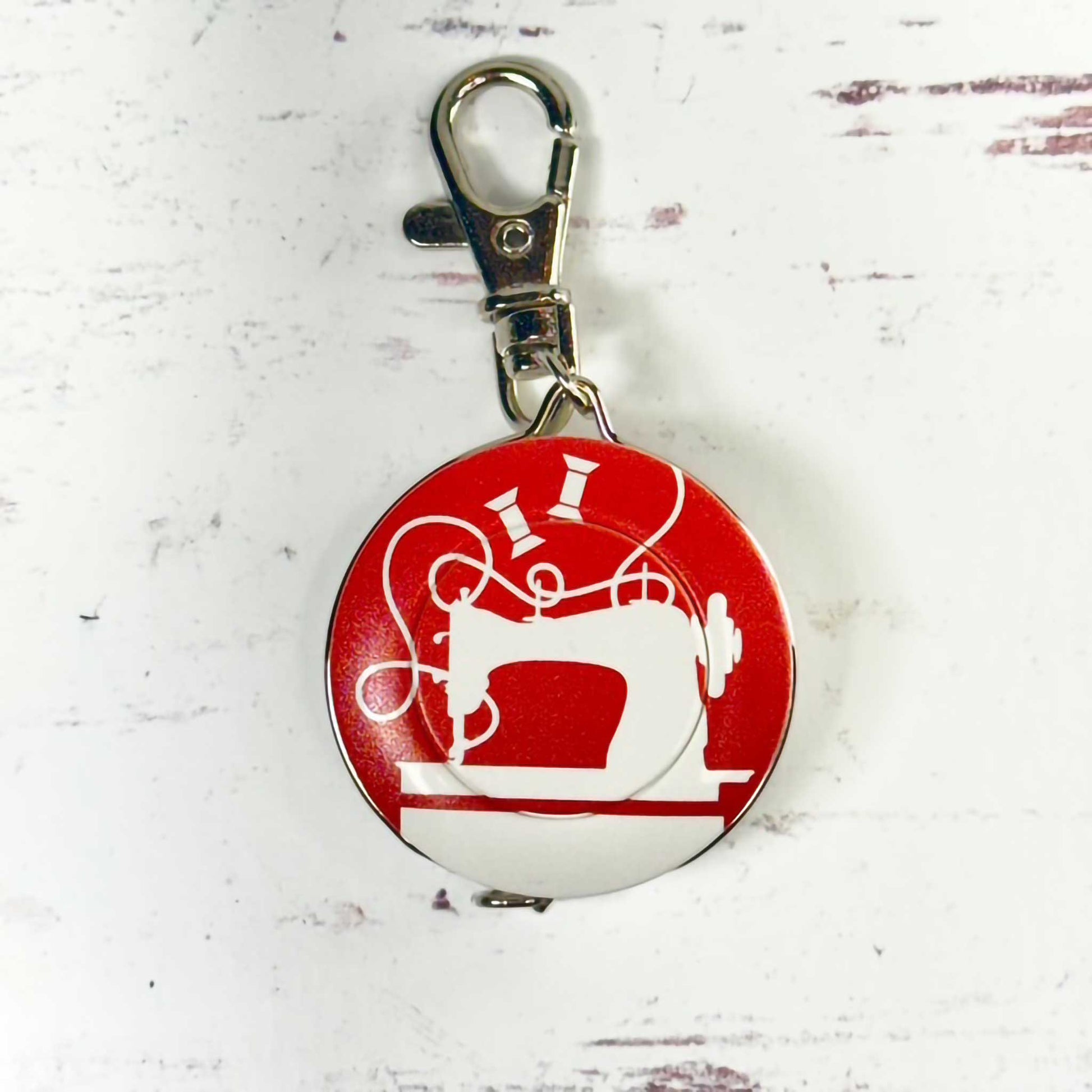 round tape measure/keychain with sewing machine design on a red background