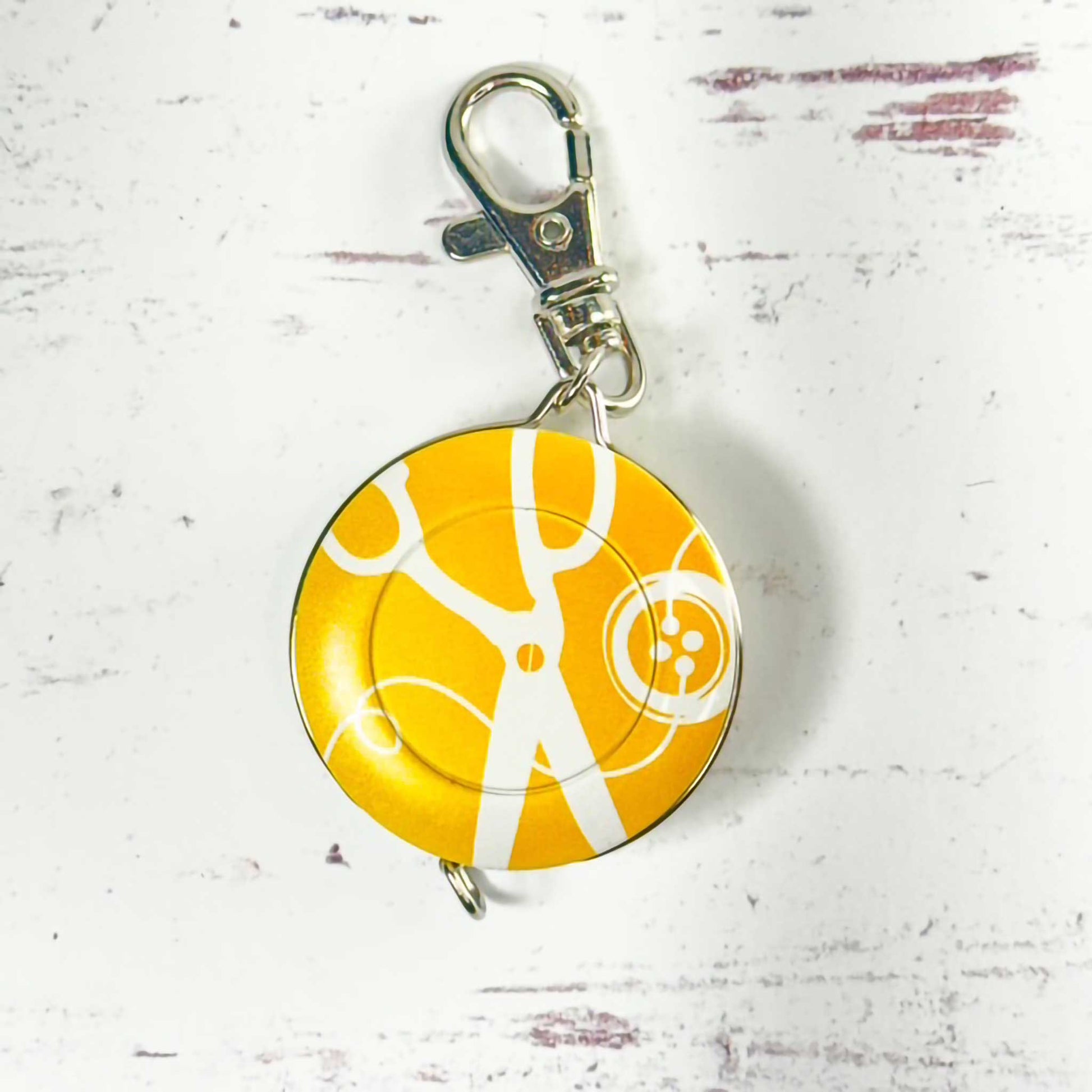 Yellow and white circular tape measure/keychain with a metal clasp on a textured white background