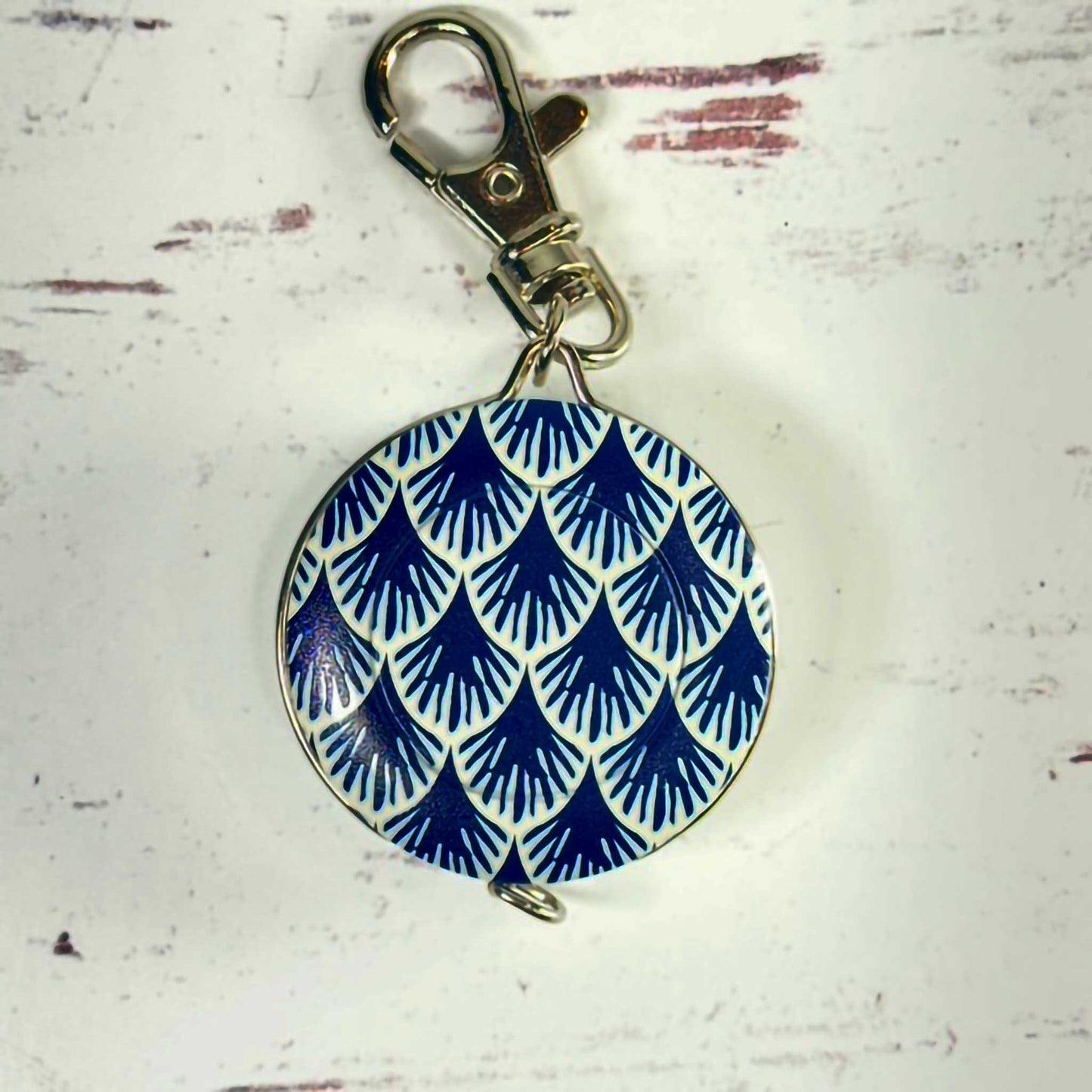 blue and white circular tape measure/keychain with a metal clasp on a textured white background