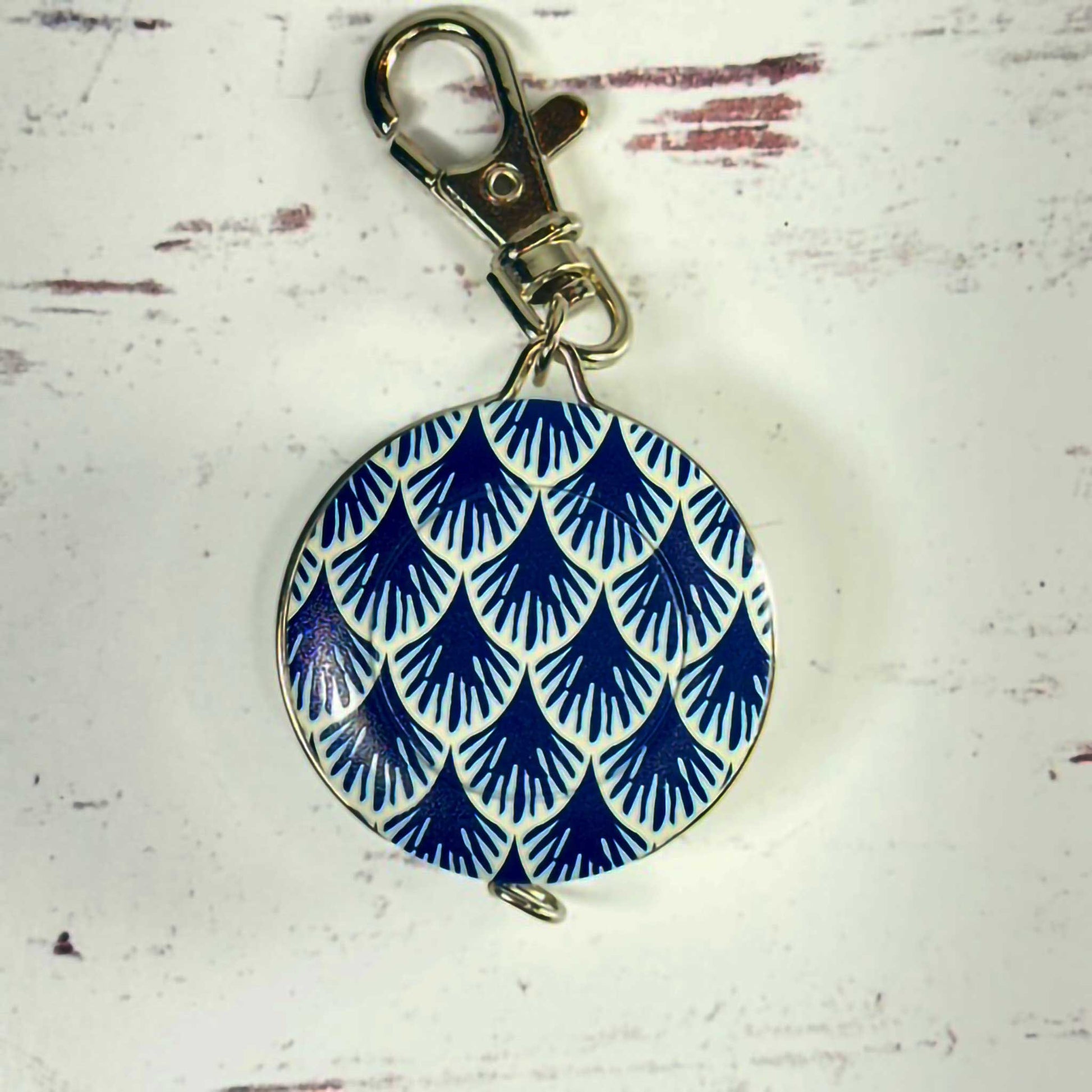 blue and white circular tape measure/keychain with a metal clasp on a textured white background