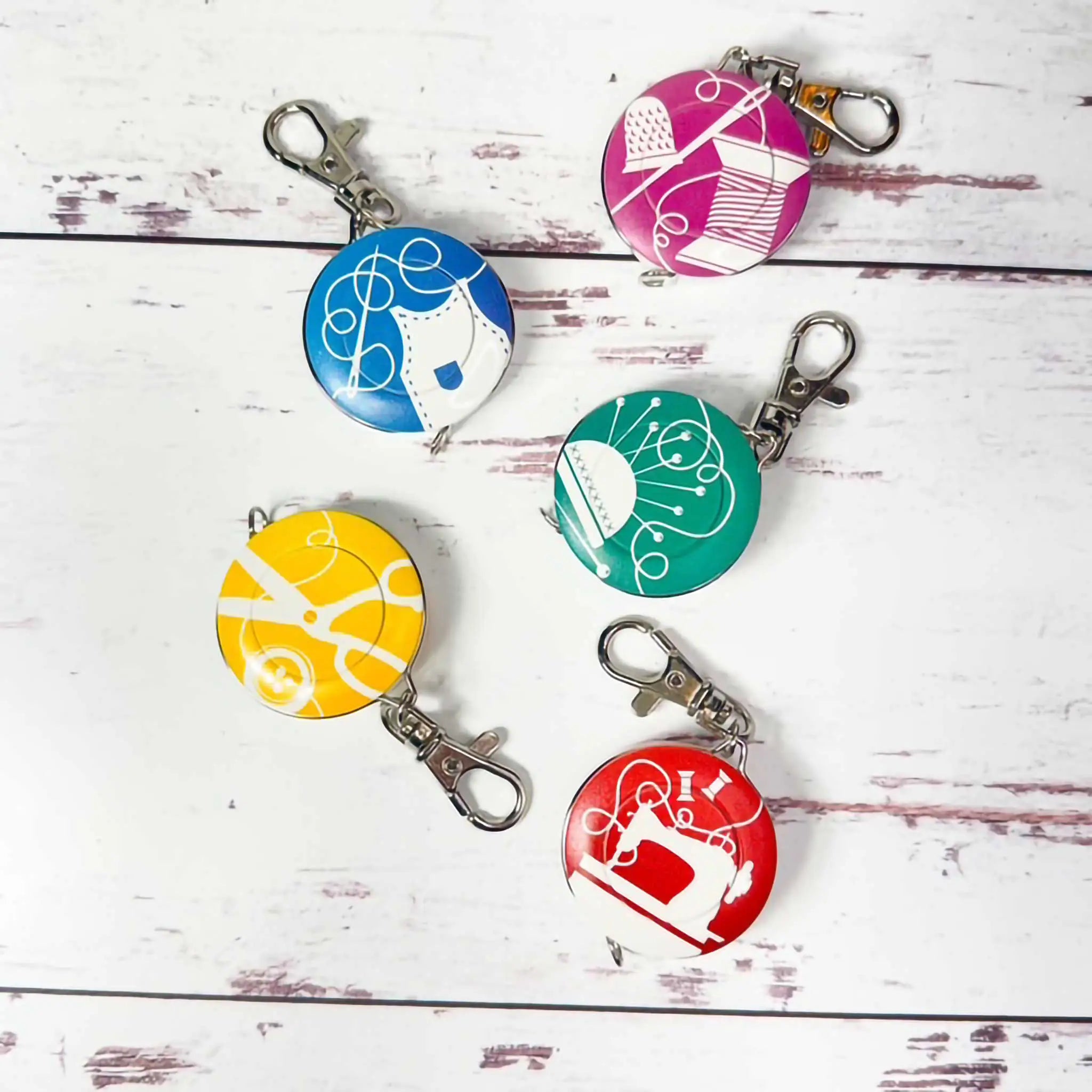Five colorful tape measures with different designs on a white wooden surface