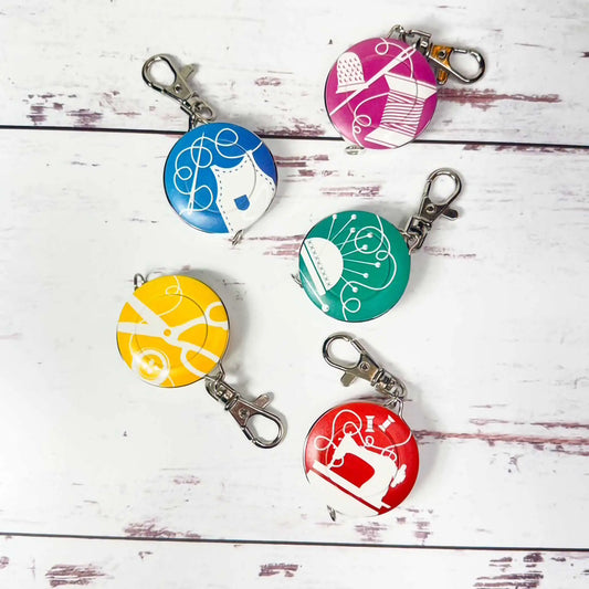 Five colorful tape measures with different designs on a white wooden surface