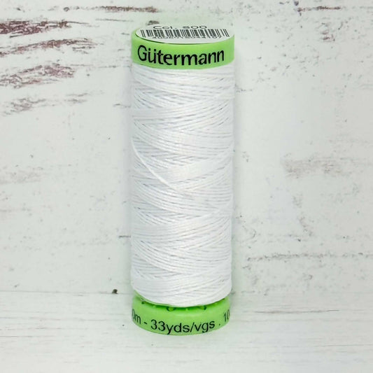 Spool of white top stitch thread with a green label on a light wooden background