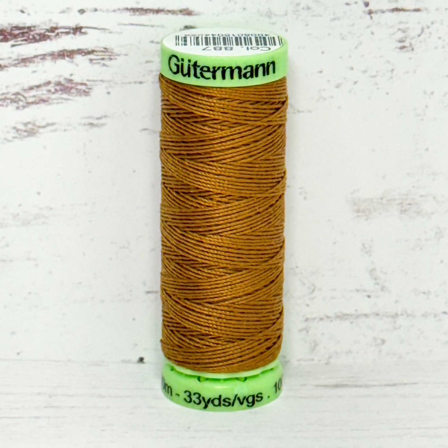 Spool of Gutermann brown top stitch thread on a light wooden surface