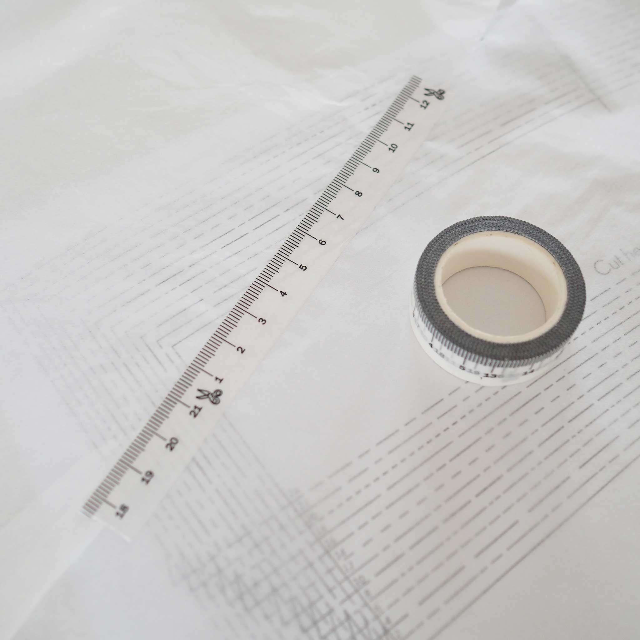 a spool of washi tape viewed from the top and a strip of tape diagonally above it.  The tape is white with black ink measuring centimeters