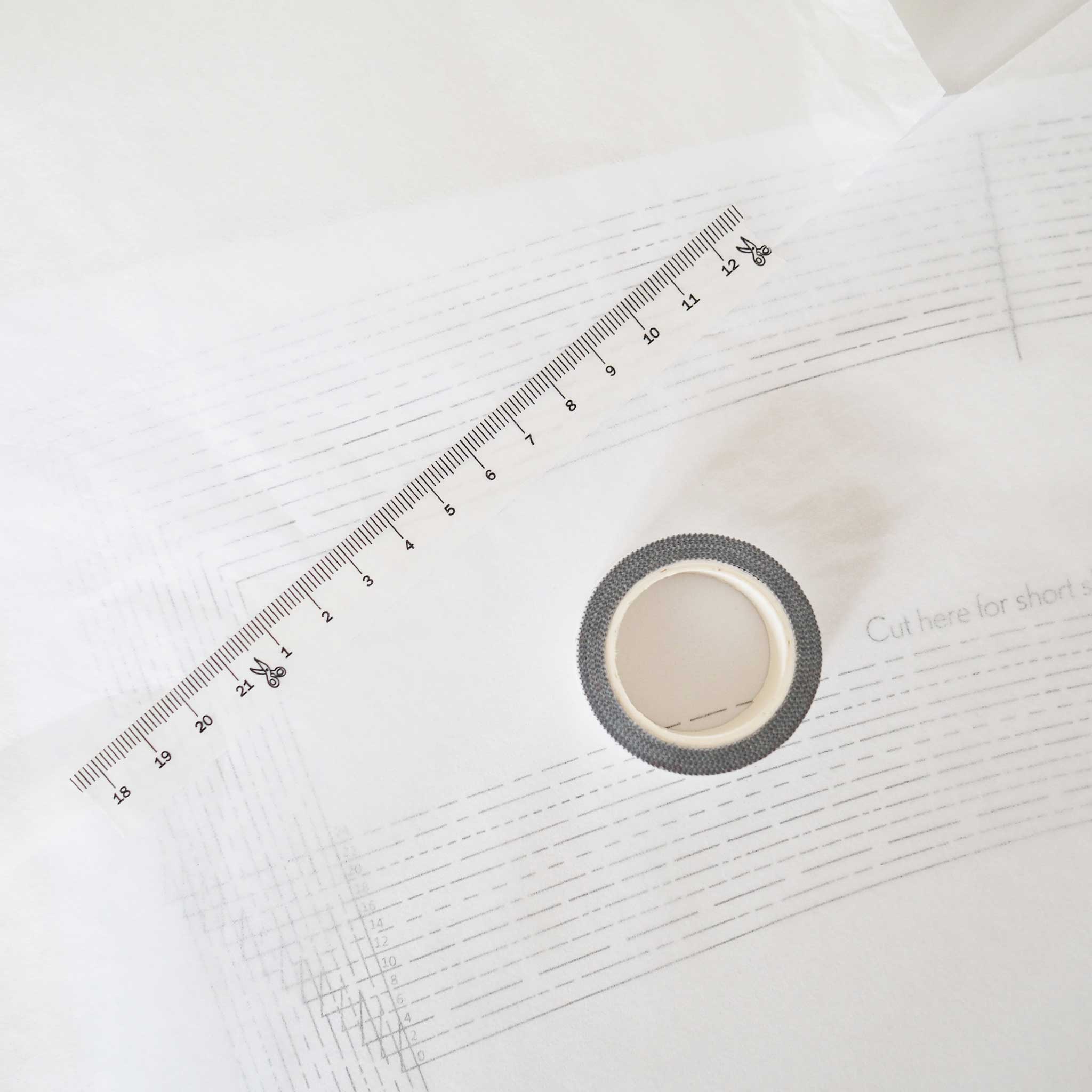 a spool of washi tape viewed from the top and a strip of tape diagonally above it.  The tape is white with black ink measuring centimeters