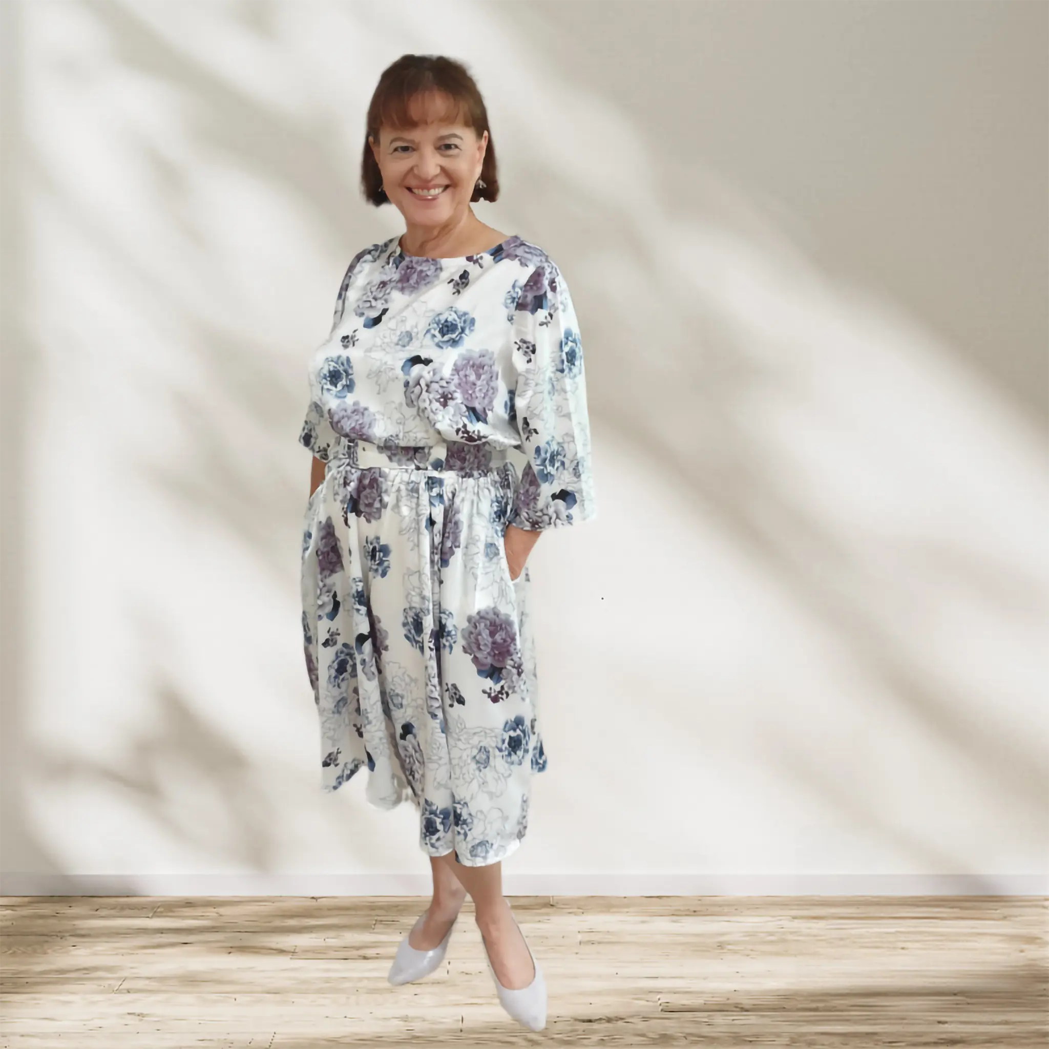 Woman wearing a floral dress standing against a plain background