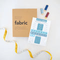 A brown paper bag colored book that says "my fabric stash" and a page of stickers that are shades of blue on a white background that describe the  seasons and occasions to wear clothing.  There is a yellow and white tape measure on the lower left corner and red and blue spools of thread in the upper right corner