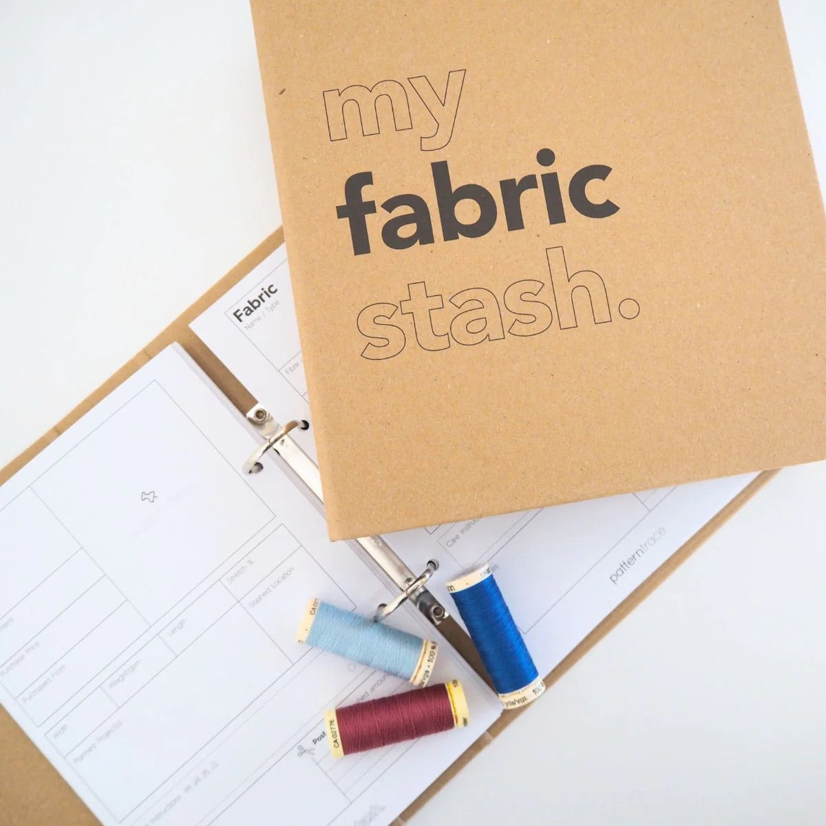 A brown paper bag colored book that says "my fabric stash" and a page of stickers that are shades of blue on a white background that describe the  seasons and occasions to wear clothing.  There are red and blue spools of thread in the center bottom portion of the photo