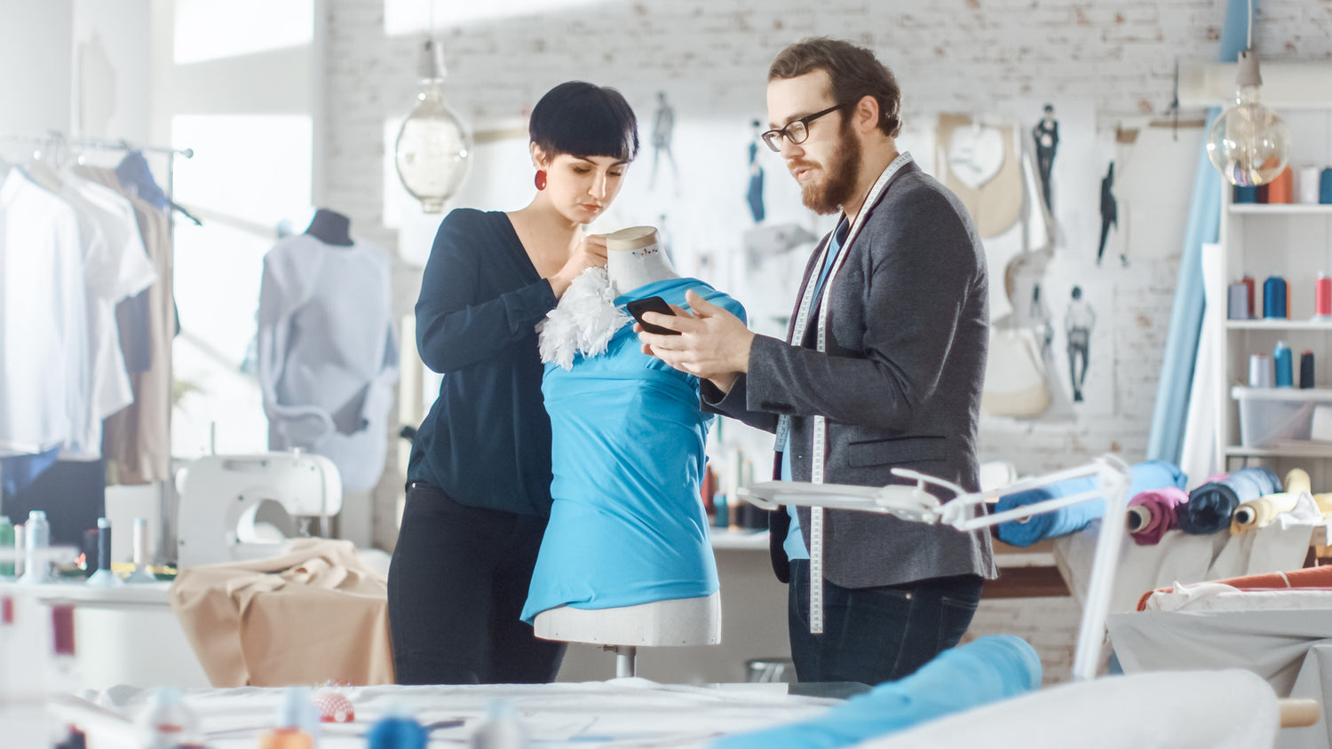 Photo of a man and woman fashion designers working on a blue t-shirt on a dress form