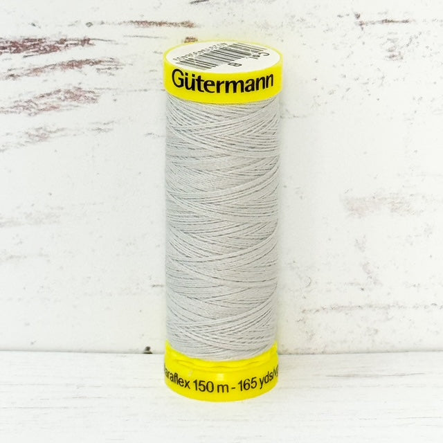 Spool of light gray Gutermann thread on a wooden surface