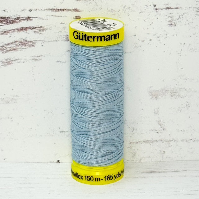 Spool of light blue Gutermann thread on a textured white background