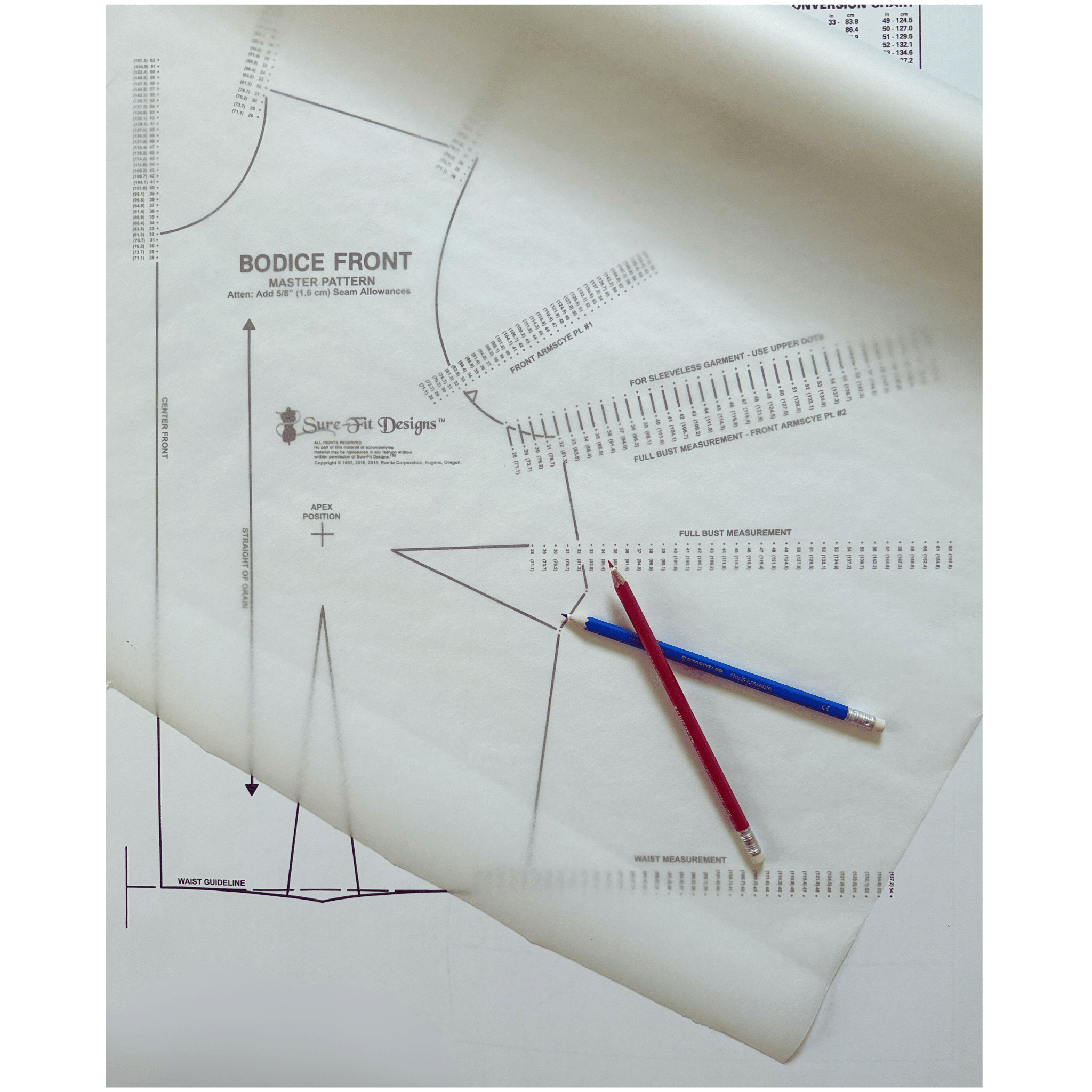a Sure Fit Designs bodice pattern with a roll of tracing vellum over the top.  There are two colored pencils one red and one blue crossed over each other on the lower right hand corner