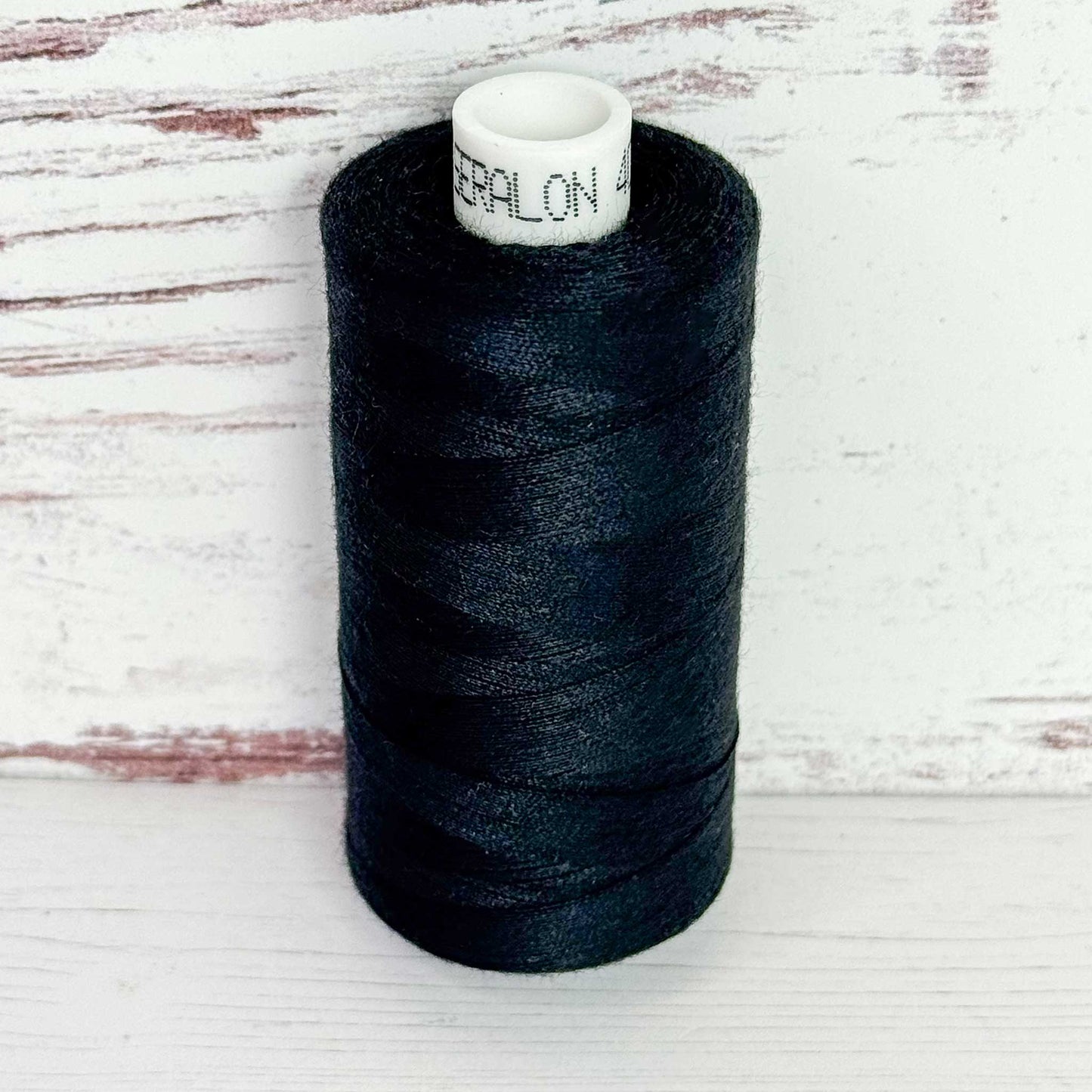 Spool of black thread with a visible brand label on a wooden surface