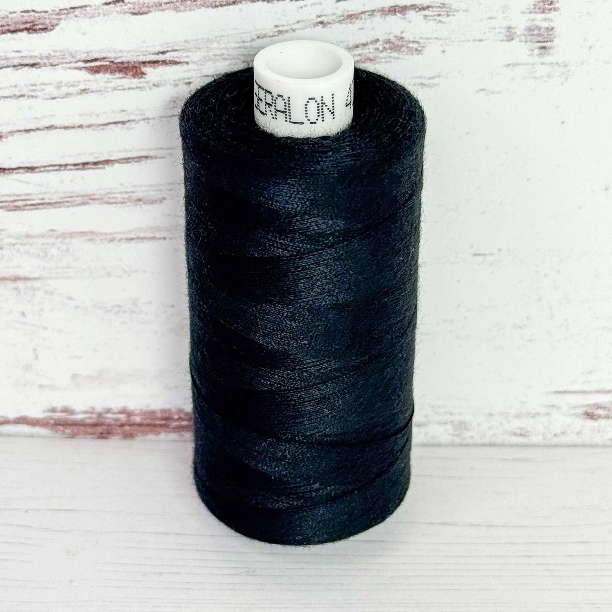 Spool of black thread with a visible brand label on a wooden surface