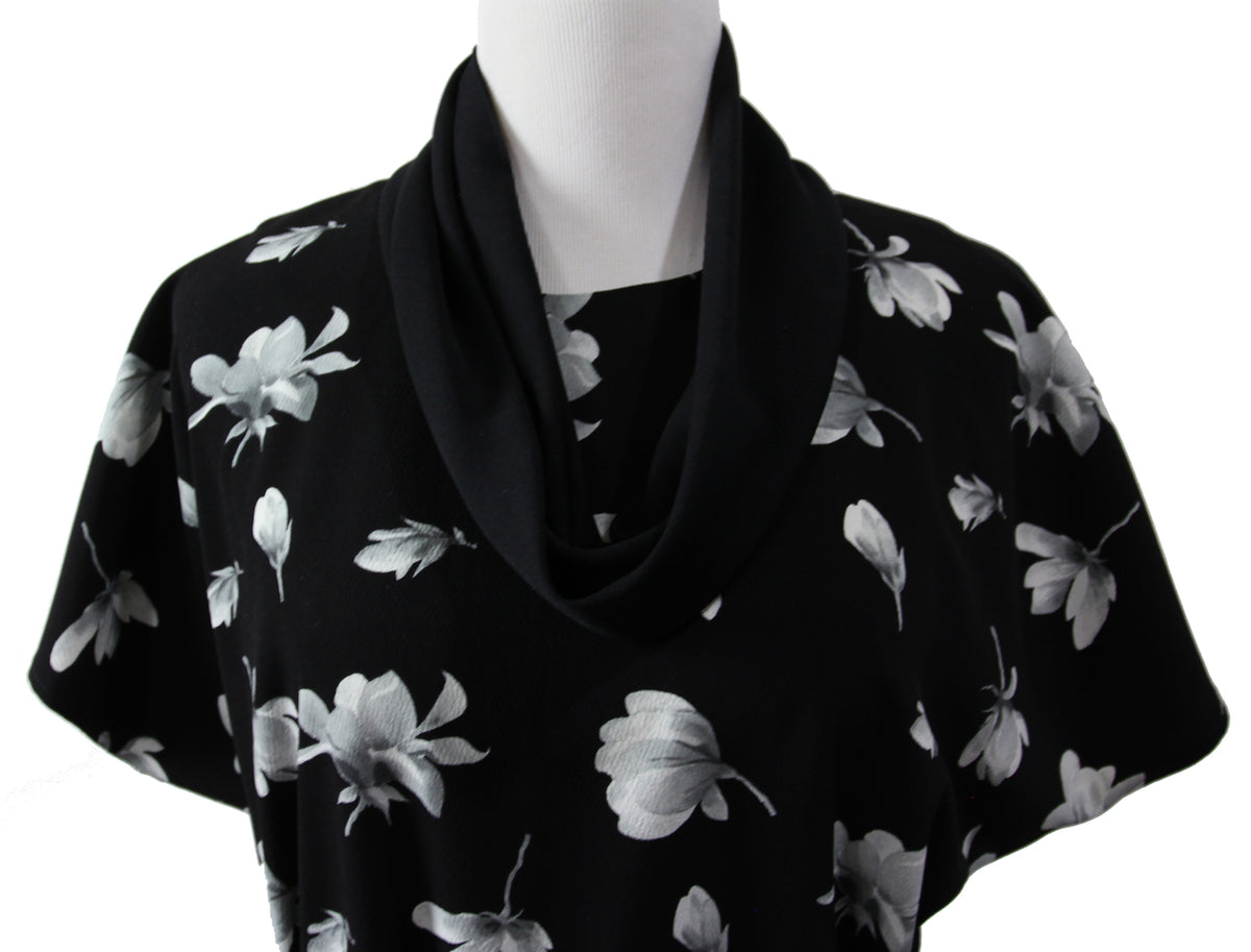 A close up of a short sleeve blouse on a mannequin. it is made of black fabric with large white and gray flowers and a black  infinity scarf